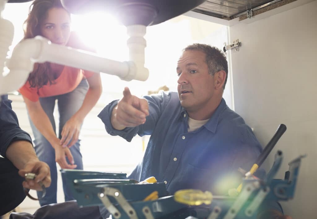 Plumber working under sink pointing to pipe